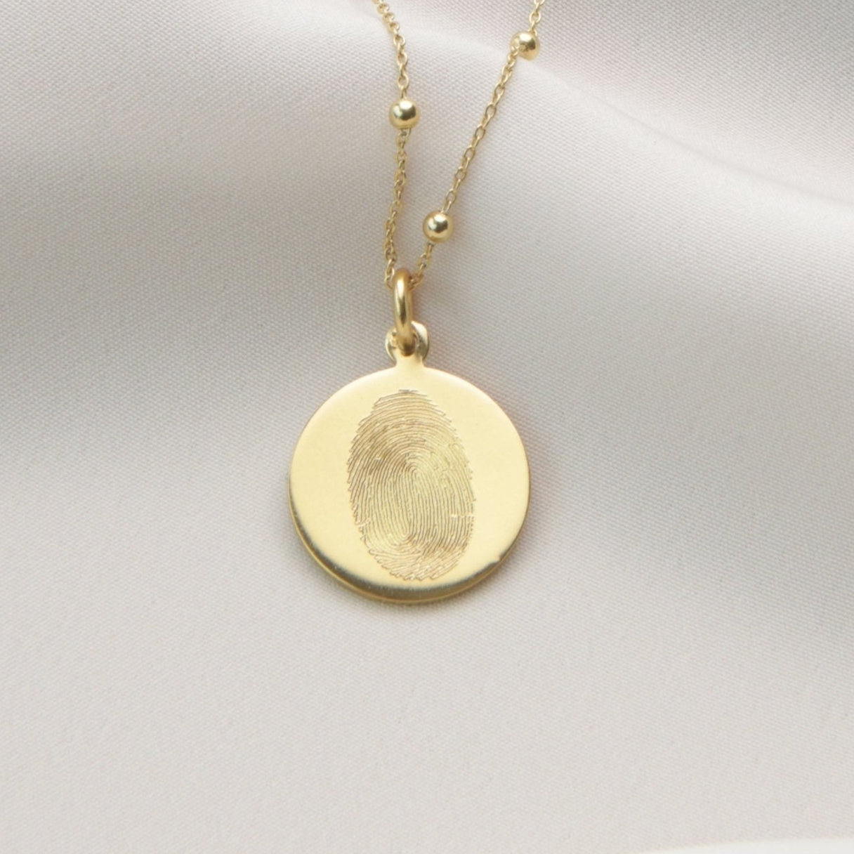 Gold necklace with a round pendant on a light gray background