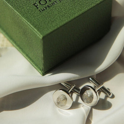 Silver cufflinks on a white surface with a green box in the background