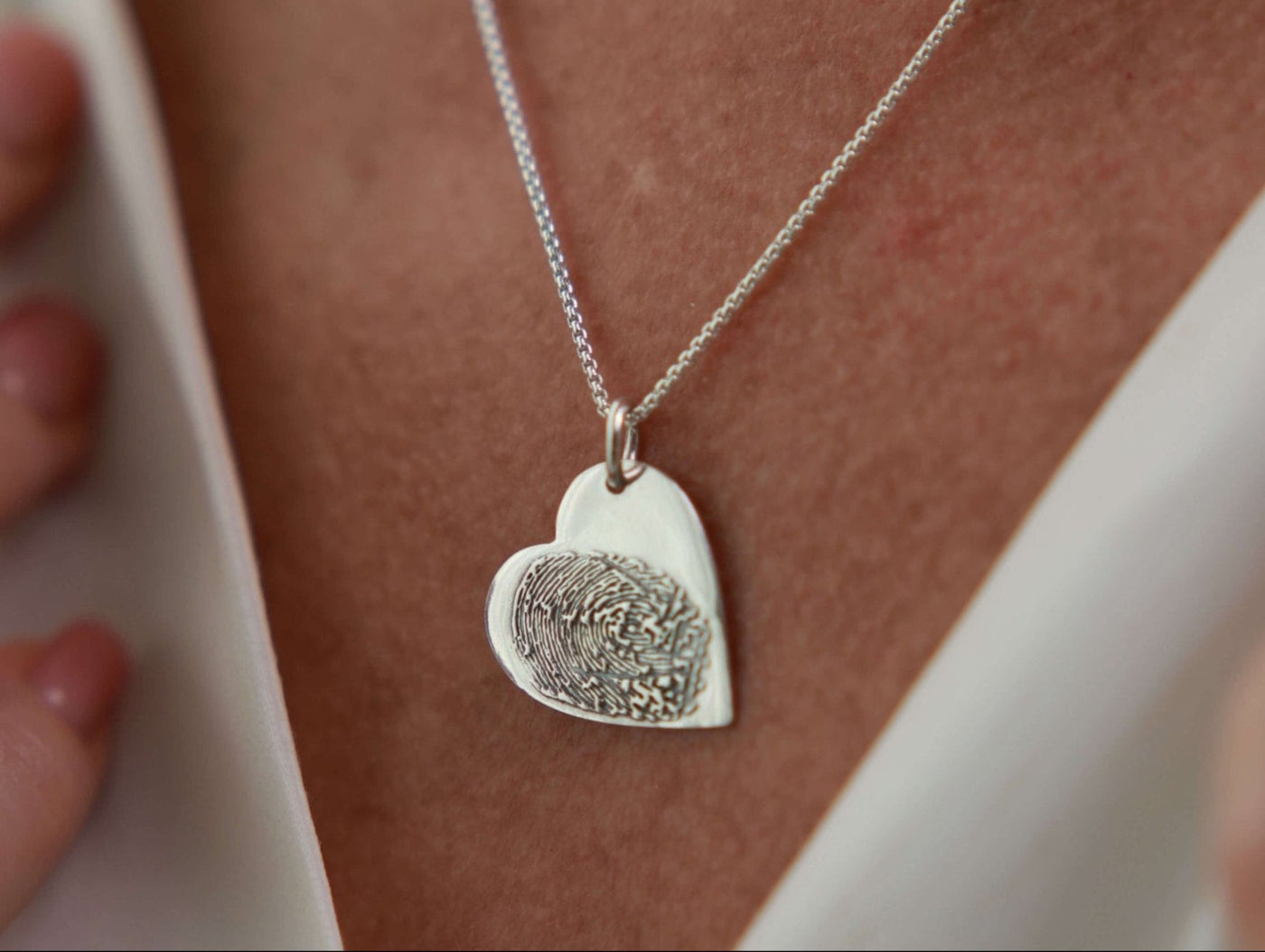Silver fingerprint in heart-shaped necklace on a person wearing a white top